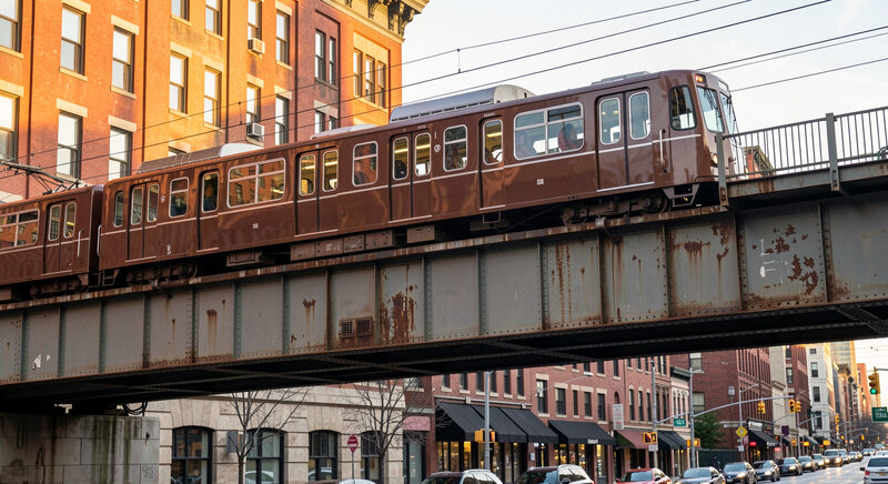 A brown steel elevated train of the Chicago Transit Authority crossing a riveted iron bridge above a downtown street, late afternoon light.